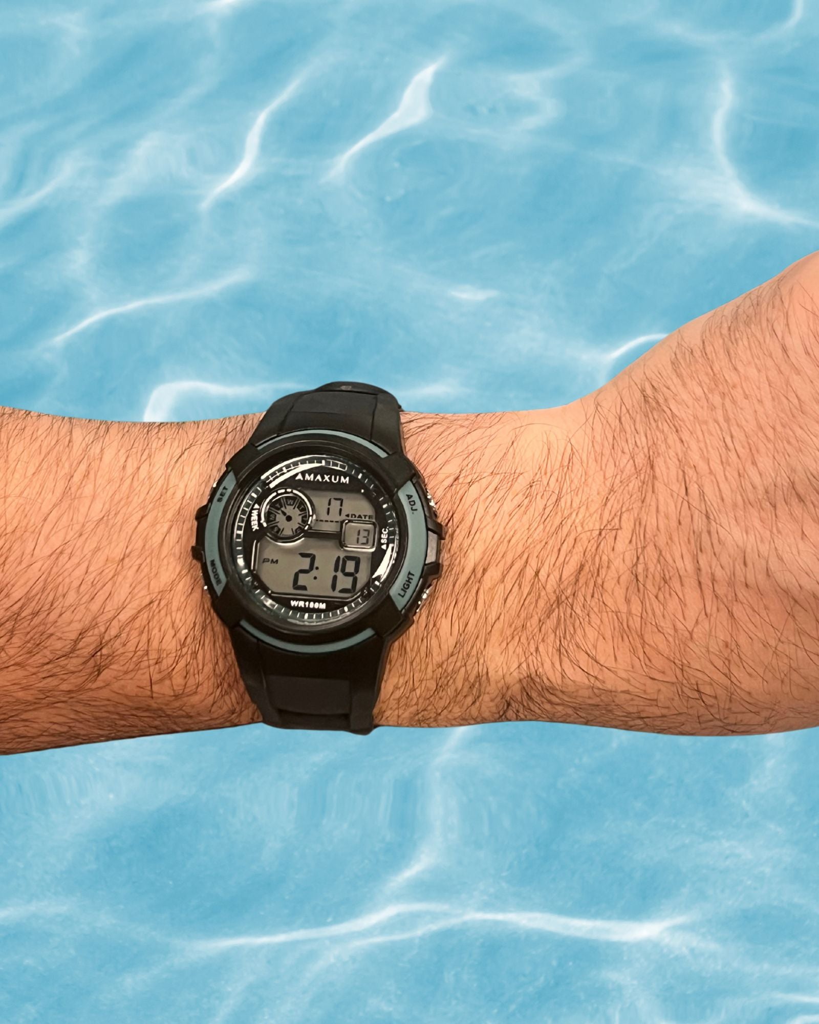 Maxum Button digital watch with a black resin strap and black case, featuring blue accents and a digital display on mans wrist