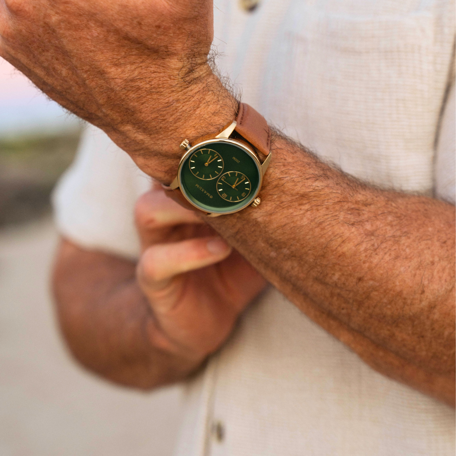 Close-up of a wrist wearing Maxum Taylor Steele Collaboration Watch with a green dial, gold-tone case, and brown leather band,