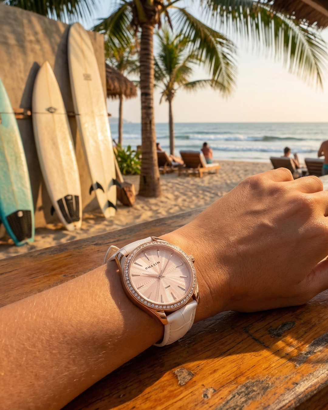 Person wearing Maxum Sydney crystal rose case and white leather strap watch with a beach and palm trees in the background