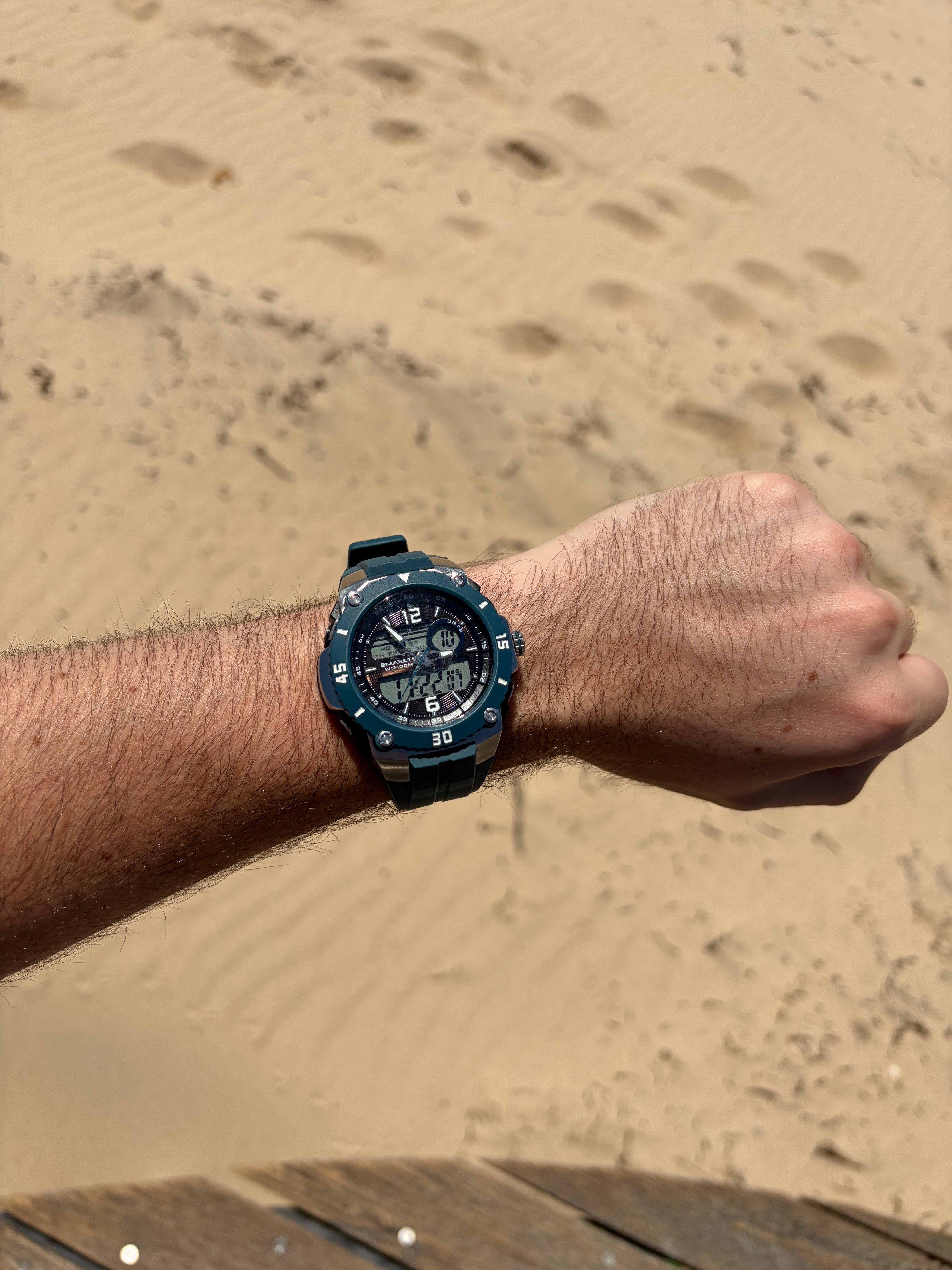 Maxum Maverick Blue Analogue Digital Watch with a silver and blue-tone case, a digital display, and a blue resin strap on Hand wearing with a sandy background