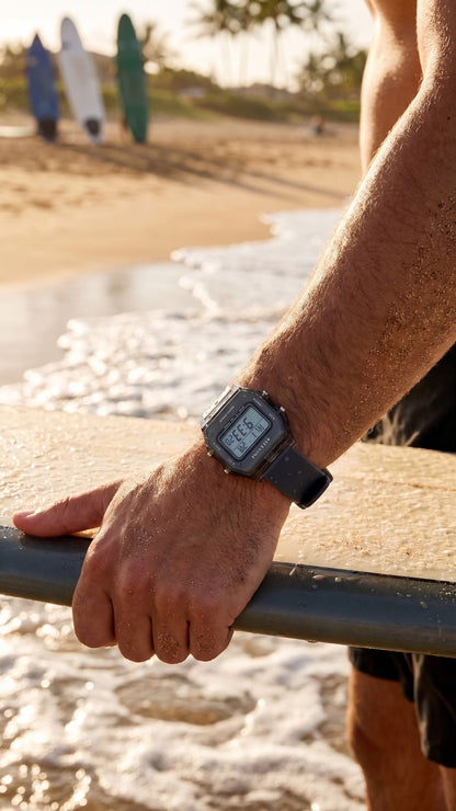 Person holding a surfboard with a digital watch on wrist at the beach