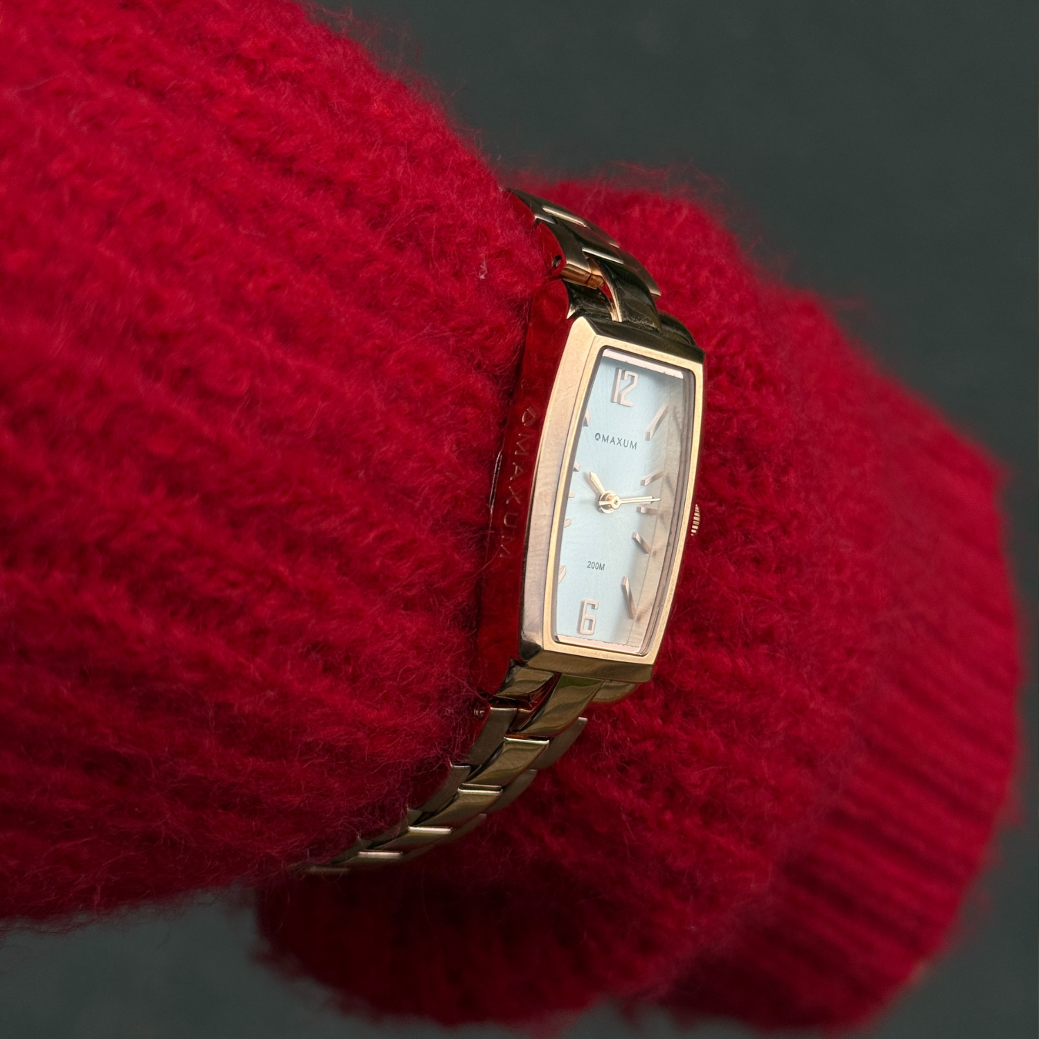 Maxum Fanta Reissue Rectangular rose gold-tone rectangular analogue watch with a white dial and a stainless steel bracelet. Close up on women's wrist wearing a red jumper