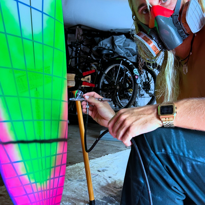 Kyuss King wearing Raglan Gold Tide Watch working on a colourful surfboard in a garage setting